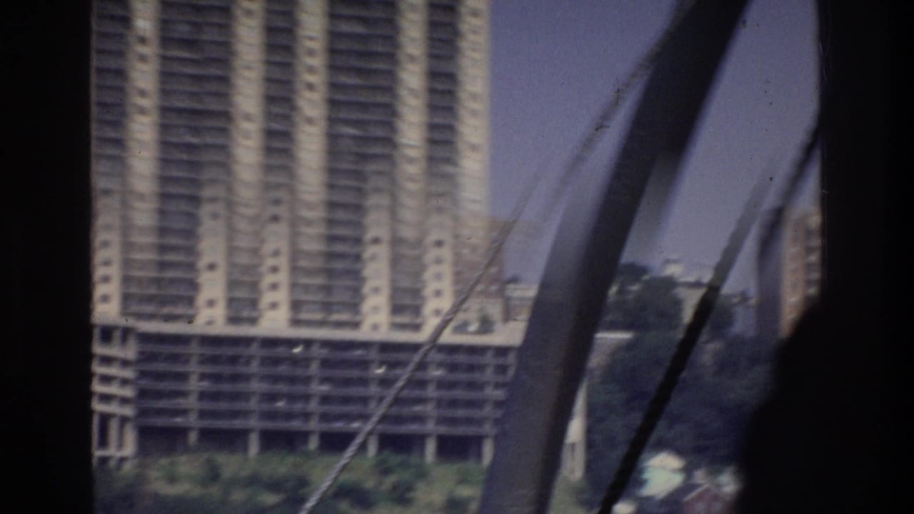 Large modernist high-rise tower seen from a boat, with rigging ropes in the foreground and a bridge arch to the right.