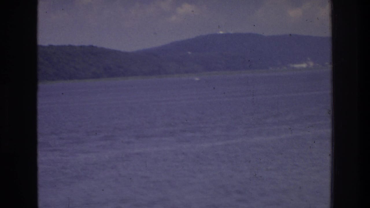 8mm home movie frame circa 1975 showing a wide expanse of calm water with a distant wooded ridge, possibly on a waterway near Washington DC.