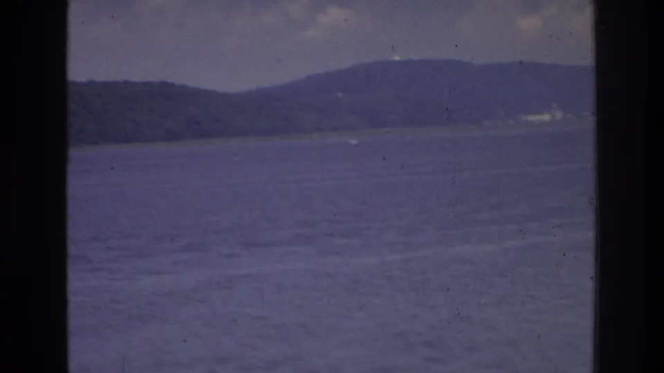 8mm home movie frame circa 1975 showing a wide expanse of calm water with a distant wooded ridge, possibly on a waterway near Washington DC.