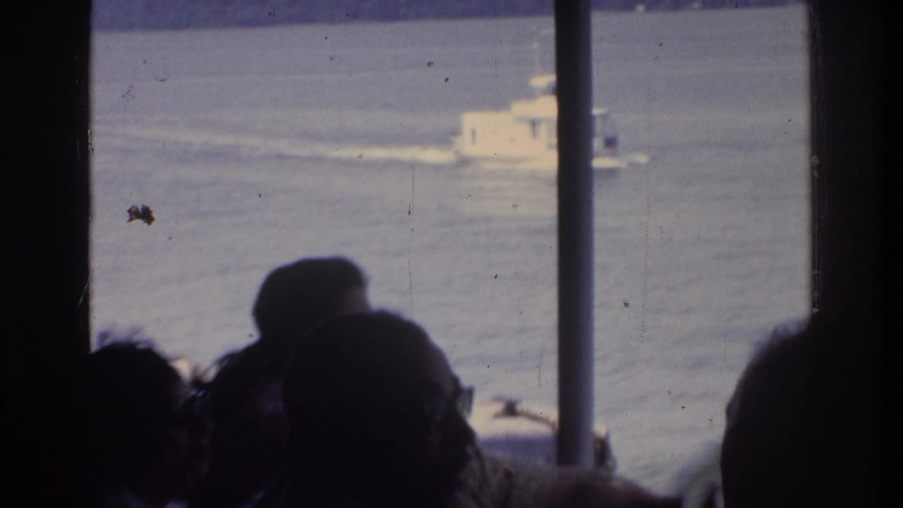 Silhouetted passengers at a ferry window watching a white motorboat, with a small unidentified object visible on the water.