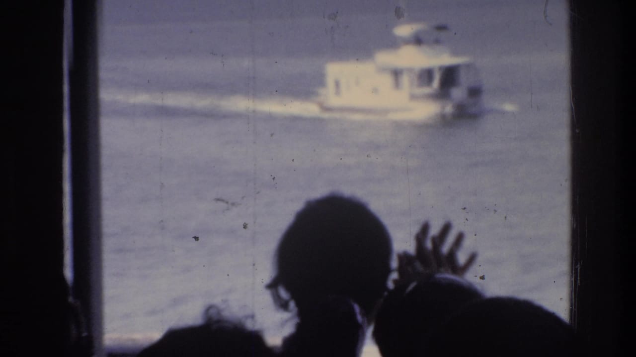 Silhouetted people waving at a passing white motor vessel, possibly on a DC-area river, circa 1975; captured on 8mm home movie film from inside a vehicle.