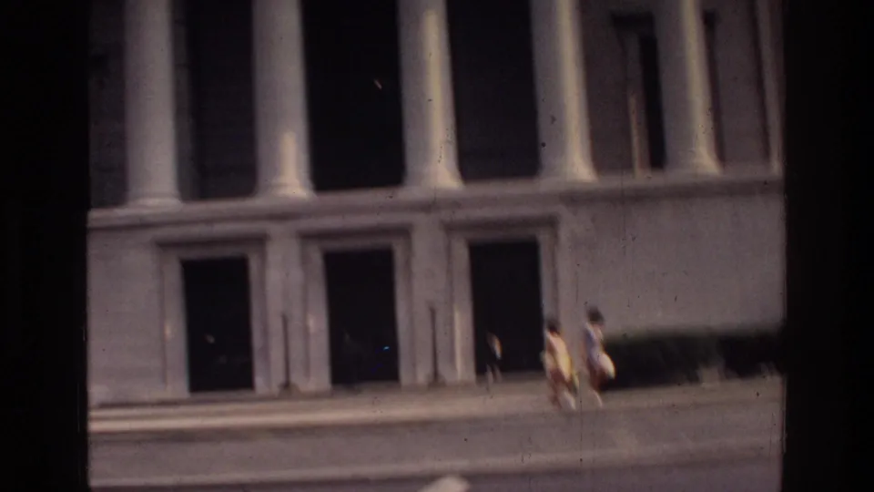 A federal-style classical building with columnar stone facade photographed from a moving vehicle in Washington DC, circa 1975, on 8mm film.