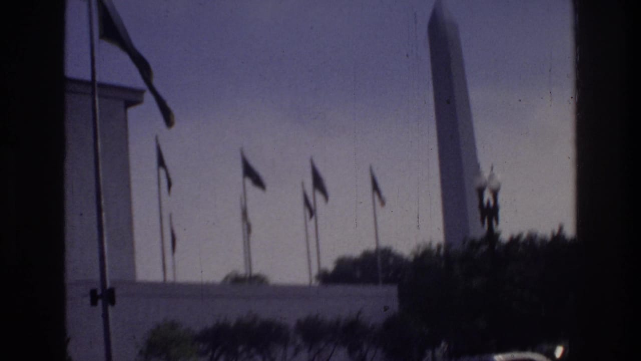 Washington Monument with row of flags and globe lamp cluster, pale sky, seen through window opening