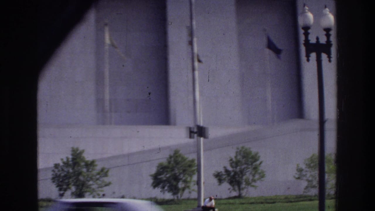 Large stone government building facade, cast-iron street lamp, and a 1970s sedan in Washington DC circa 1975, viewed through a window.