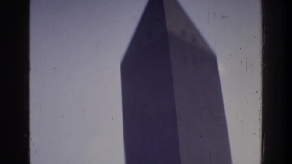 Low-angle 8mm home movie shot of the Washington Monument upper section and pyramidion apex circa 1975, Washington DC, against blue-gray sky
