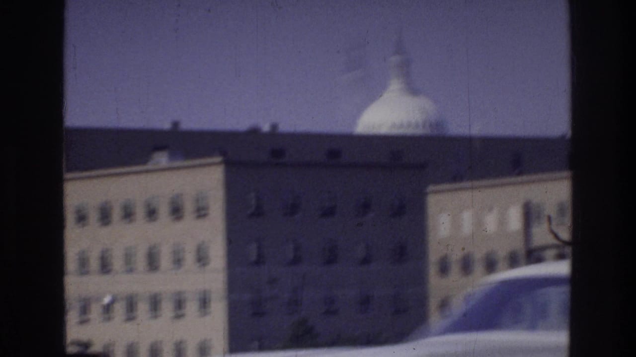 8mm home movie POV from a moving car in Washington DC, 1975, showing what appears to be the U.S. Capitol dome rising above a large federal building through the car window.