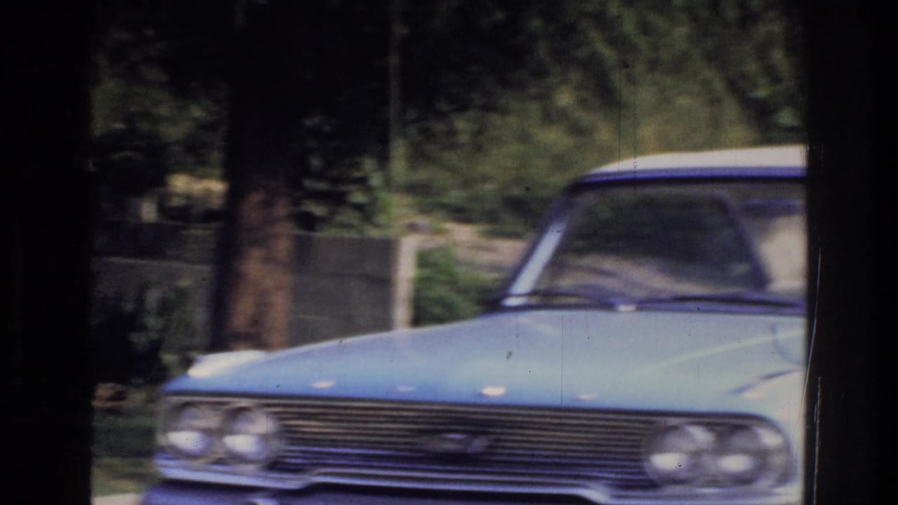 Front-facing view of a light blue American sedan with chrome grille and quad headlights, likely a late-1950s or early-1960s model, 8mm home movie, Washington DC area, circa 1975.