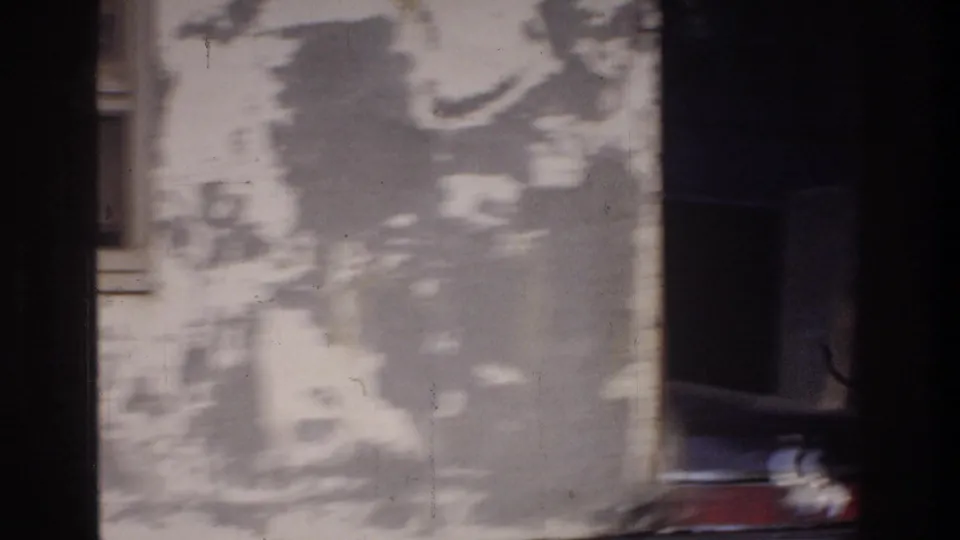 Close-up of a deteriorating stucco or plaster wall with extensive paint peeling, 8mm home movie fragment, Washington DC area, circa 1975.