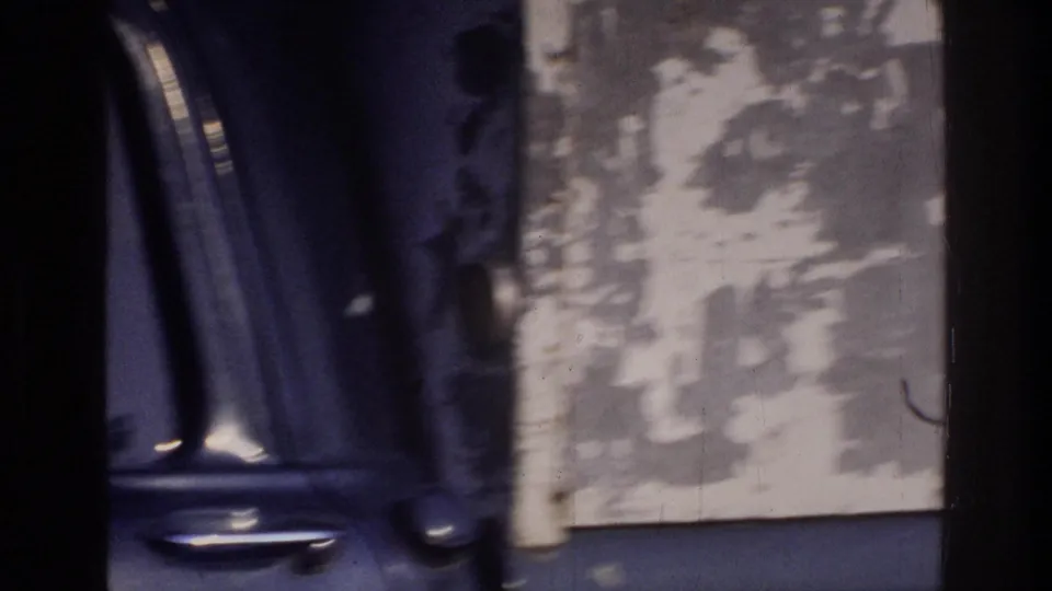 Dark car door framed against a heavily weathered peeling stucco wall with a partial human figure below, 8mm home movie, Washington DC area, circa 1975.