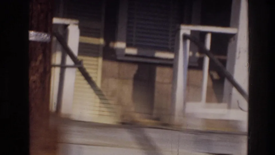 White-railed front porch with exterior stairs and shuttered windows on a residential house, Washington DC area, circa 1975, captured mid-pan on 8mm film.