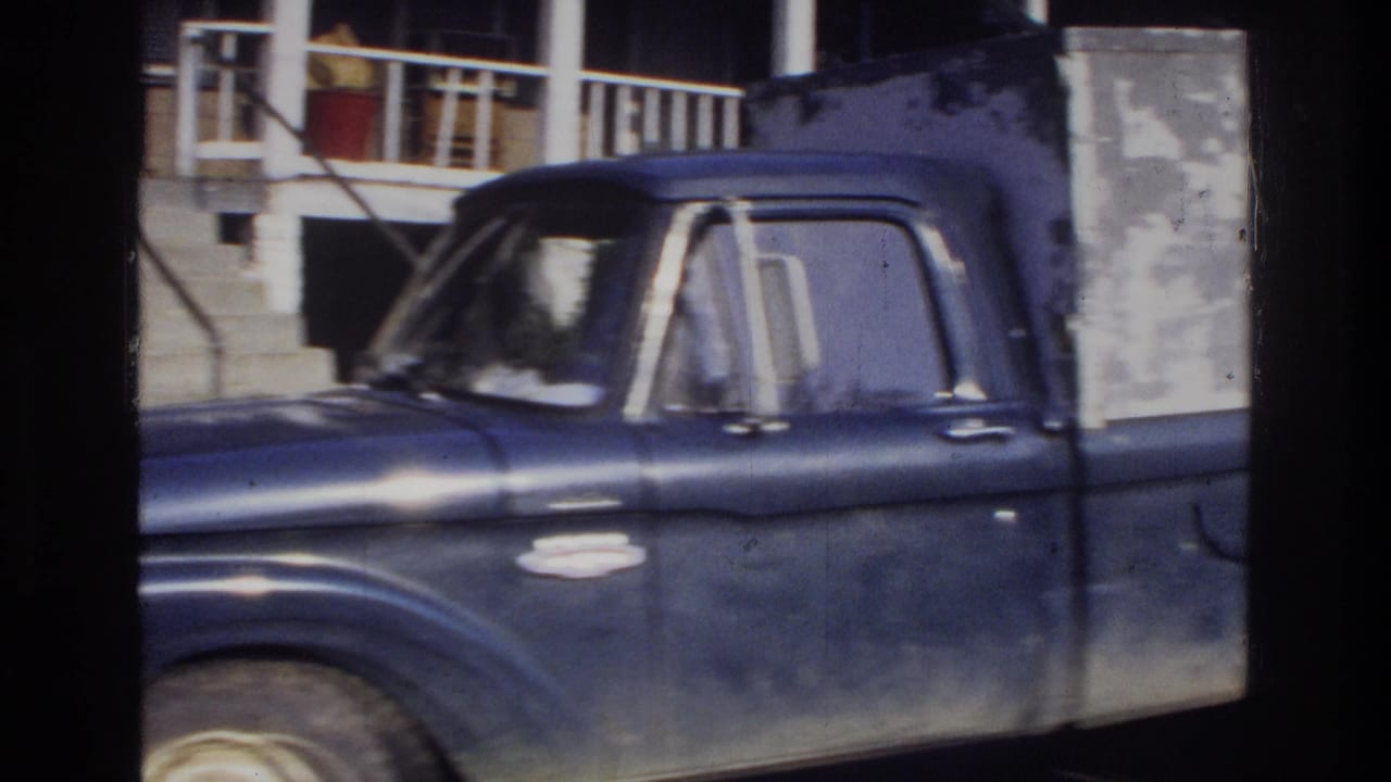 Close-up of a worn dark-blue American pickup truck with utility box, shot through a window frame; consistent with mid-1970s 8mm footage from the Washington DC area.