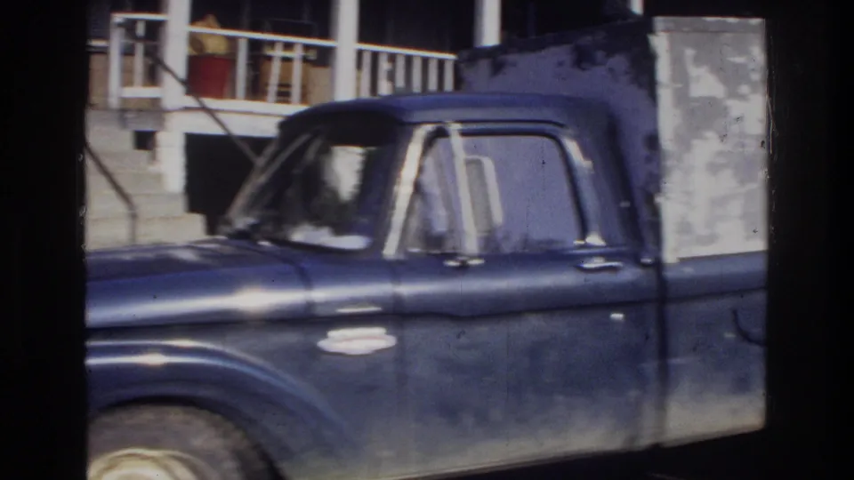 Close-up of a worn dark-blue American pickup truck with utility box, shot through a window frame; consistent with mid-1970s 8mm footage from the Washington DC area.
