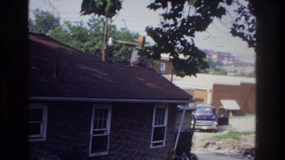 Single-story brick residential building viewed from an elevated or window vantage; trees, utility poles, and a parked period vehicle visible; consistent with 1970s suburban Washington DC area.