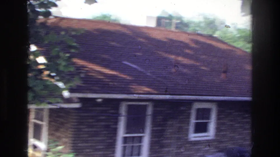 Worn red-brick residential exterior with aged shingles and double-hung windows; 8mm color fading and grain visible; consistent with mid-1970s Washington DC suburban footage.
