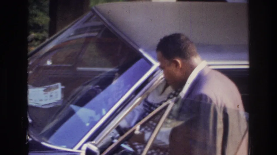 Well-dressed Black man prepares to enter a large 1970s American sedan with the door open; Washington DC home movie, circa 1975.