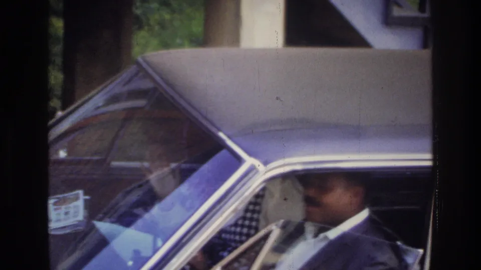 The driver appears low in the front seat, partially hidden by the side window frame and reflections on the sedan glass.