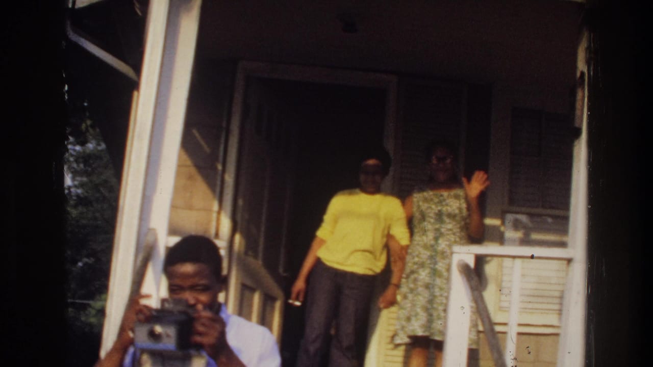 1975 Washington, DC 8mm frame showing two adults on a porch while a man in the foreground appears to hold a camera.