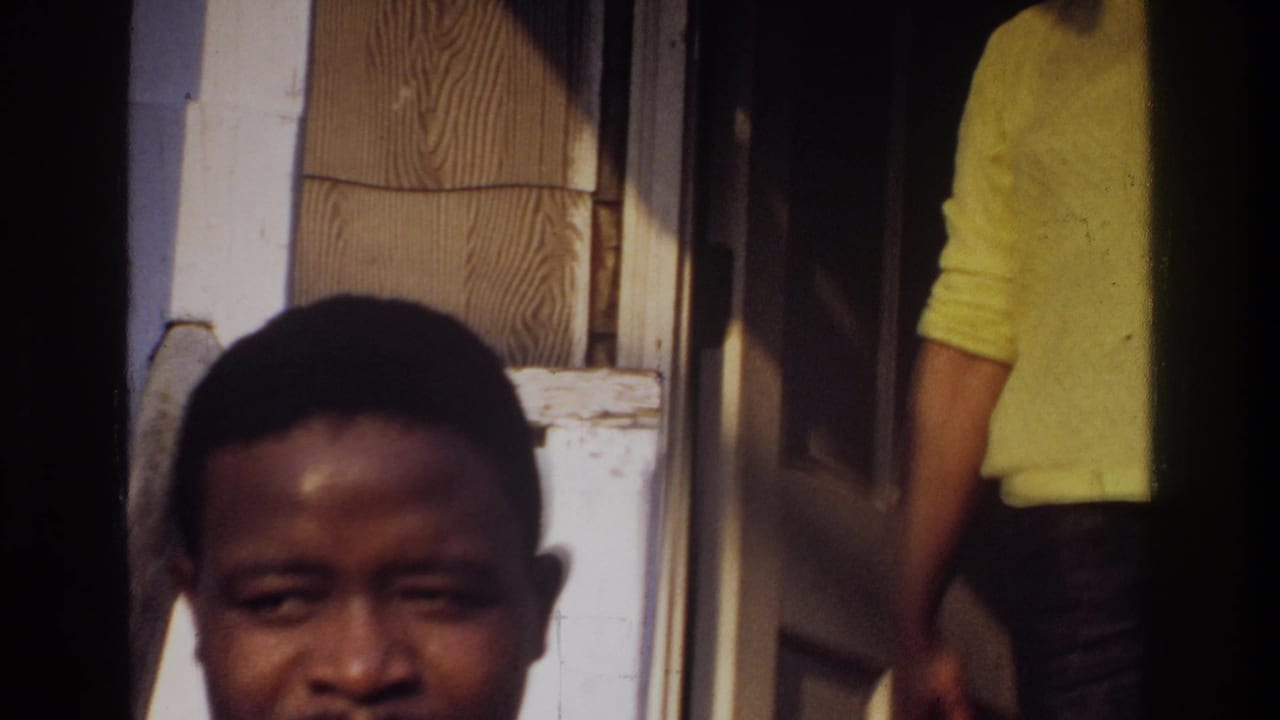 1975 Washington, DC home-movie frame with a young man close to the camera near a house entrance and a partly visible person in yellow.
