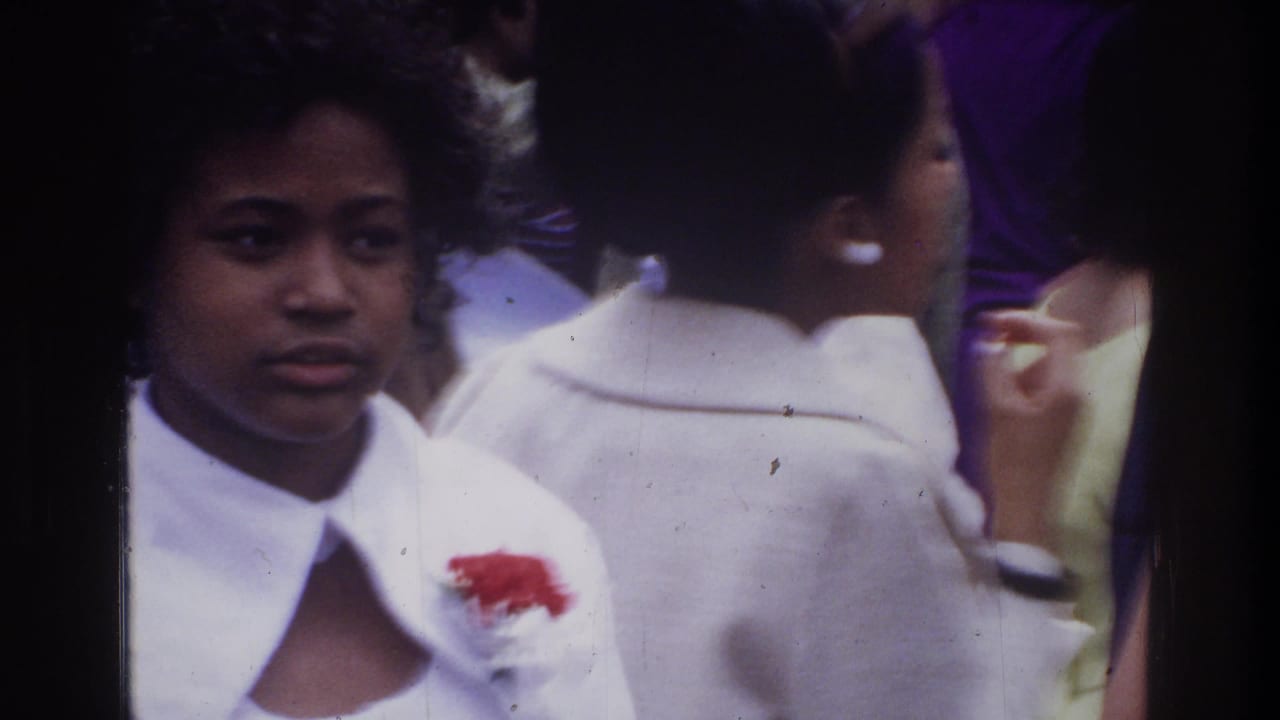 Woman in a white blouse with a red flower pin among people.