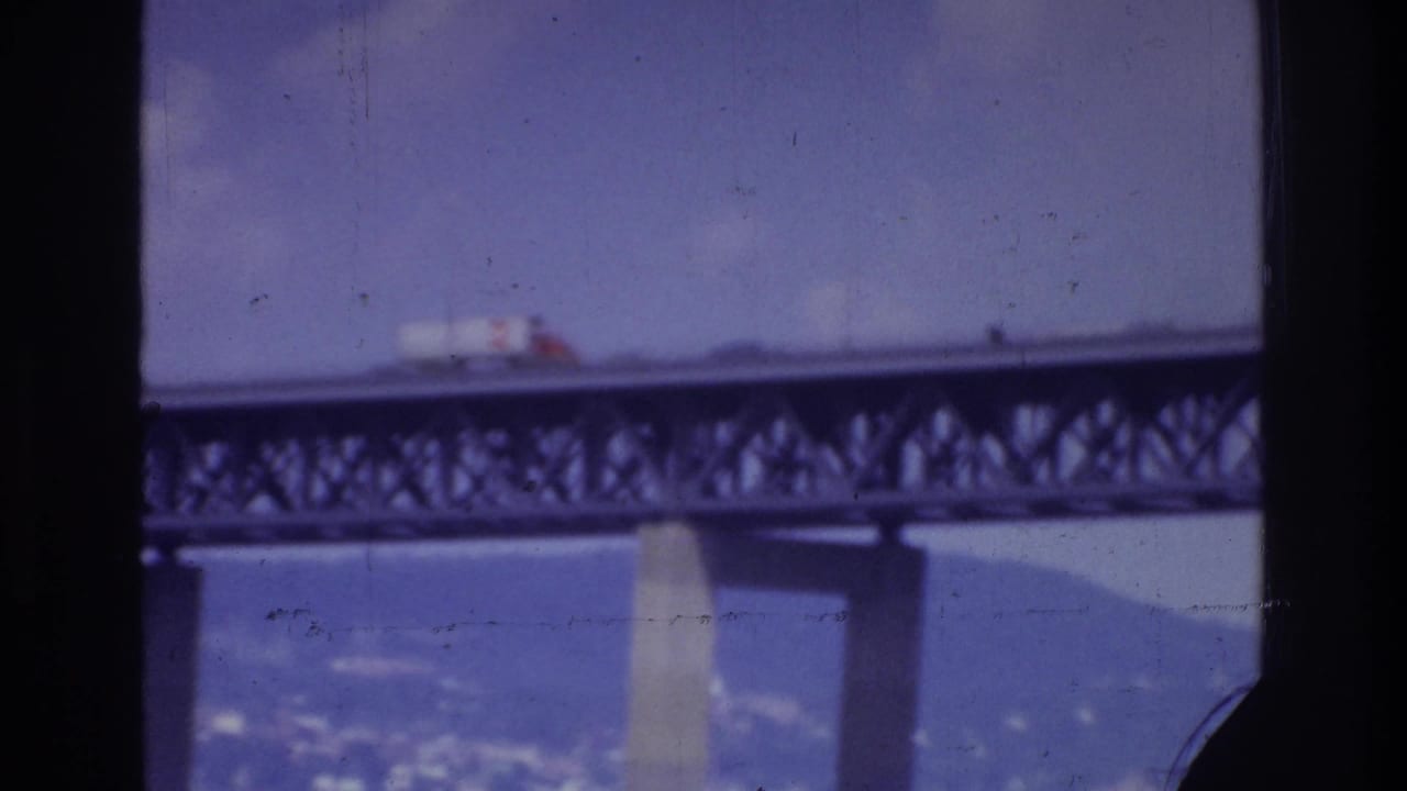 White truck on a bridge span, partially divided by a dark vertical foreground frame.