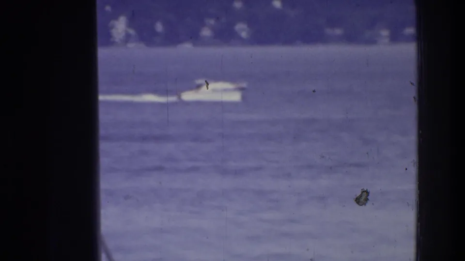 A small white boat moves across open water in the Washington, DC home-movie scene, with dark foreground framing and visible film wear.