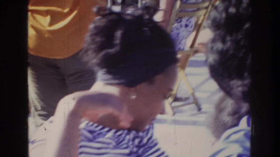 Close-up of a woman in a blue-and-white striped top at an outdoor gathering, Washington DC, 1975; gold-framed folding chairs and attendees behind her.