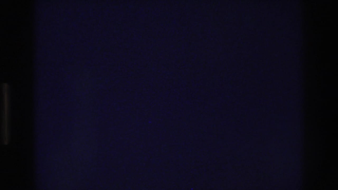 Underexposed 8mm frame from a 1975 home movie showing a deep blue-black field with faint rectangular outlines that may indicate a door or window beginning to appear.