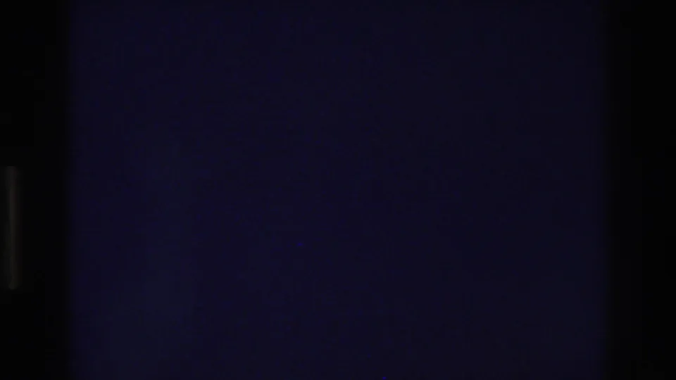 Underexposed 8mm frame from a 1975 home movie showing a deep blue-black field with faint rectangular outlines that may indicate a door or window beginning to appear.