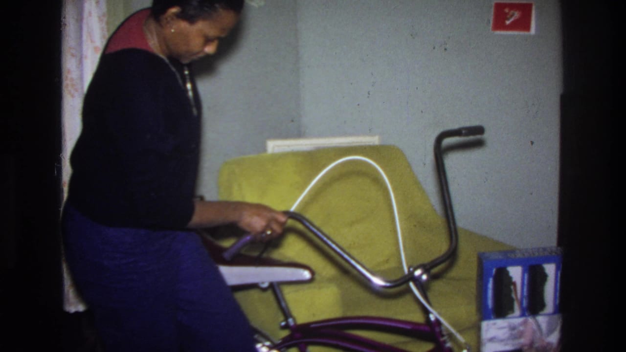Woman in dark sweater seated beside a purple banana-seat bicycle with yellow-green sofa behind her