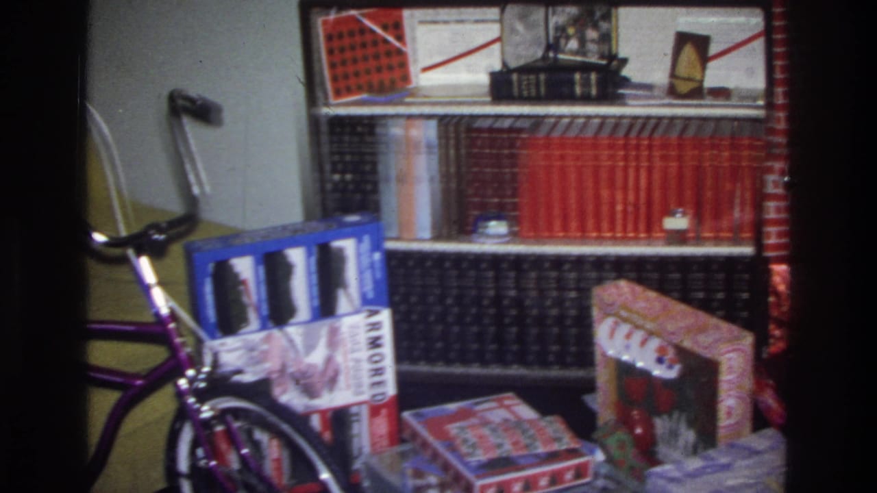 Purple children's bicycle next to wrapped gift boxes and a red encyclopedia set on a bookshelf; Washington DC home living room, circa 1975.