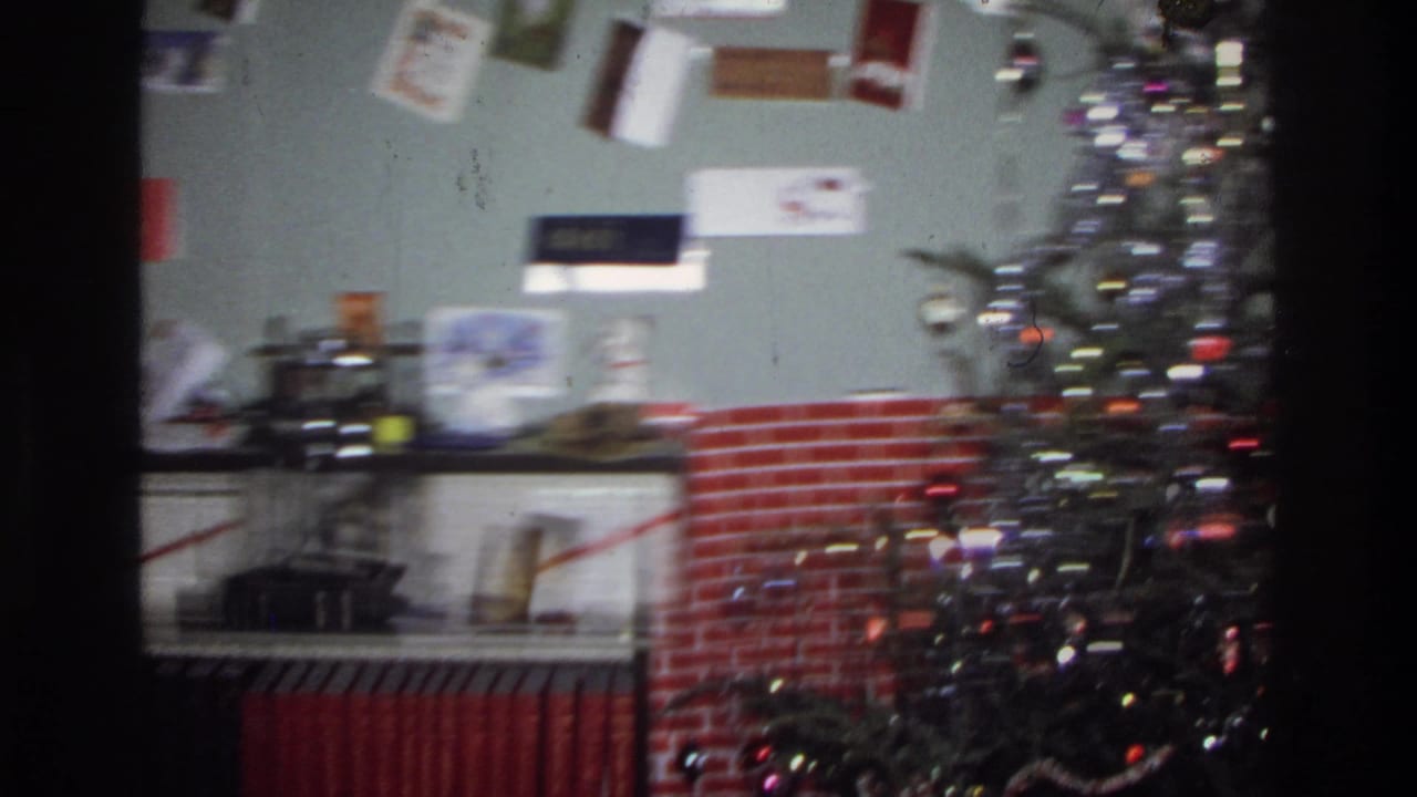 Motion-blurred pan showing a decorated Christmas tree with colored lights and a red brick fireplace surround.
