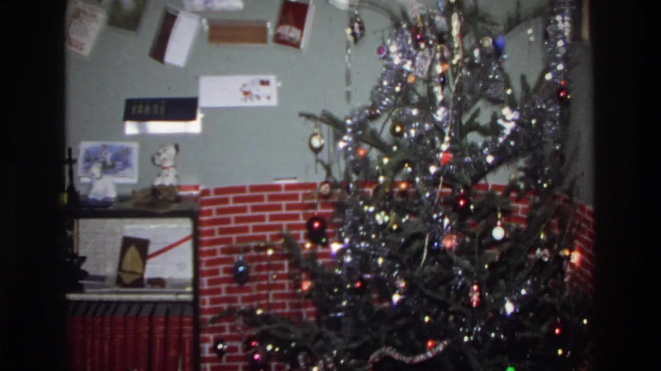 Christmas tree draped in silver tinsel and colored ball ornaments with string lights, beside a red brick fireplace surround; Washington DC home, circa 1975.