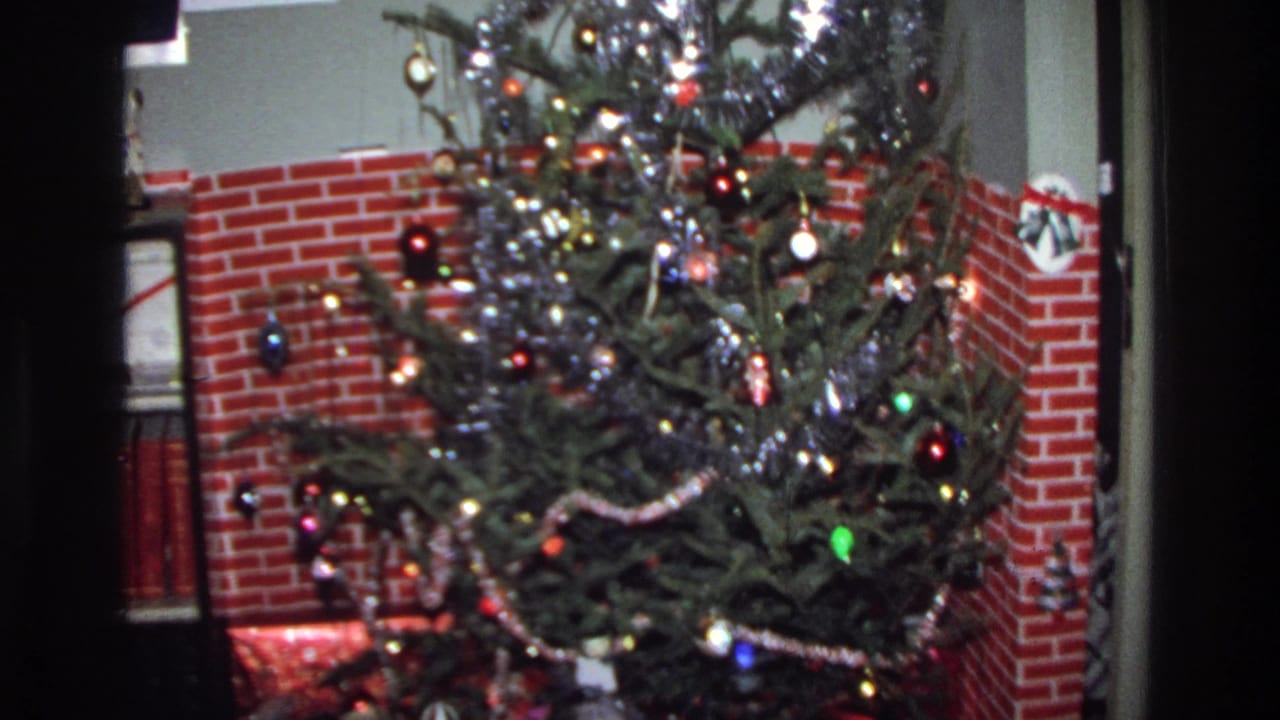 A pine Christmas tree hung with silver tinsel, colored ball ornaments, and string lights, standing before a red brick fireplace surround in a 1975 Washington DC home.