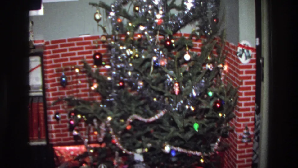 A pine Christmas tree hung with silver tinsel, colored ball ornaments, and string lights, standing before a red brick fireplace surround in a 1975 Washington DC home.