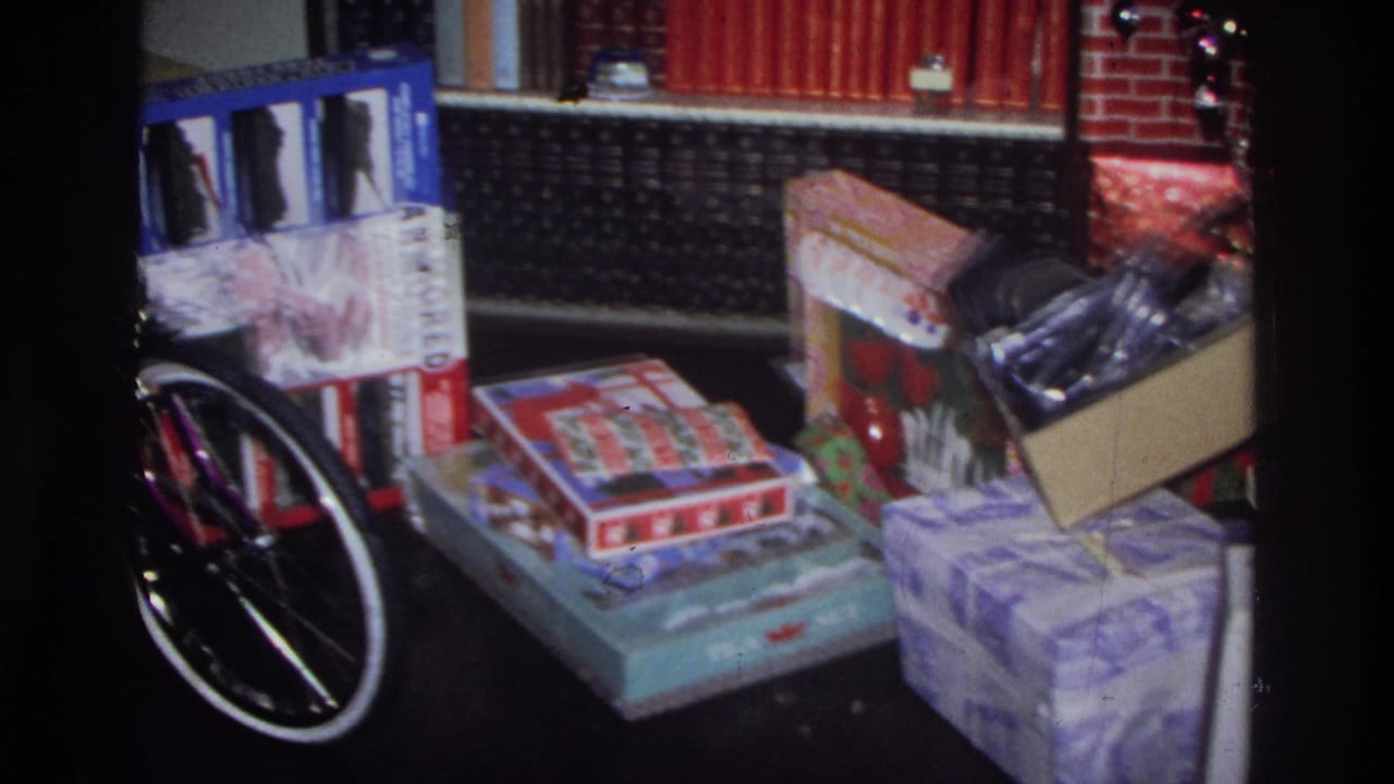 8mm home movie frame circa 1975 Washington DC: a purple bicycle wheel adjacent to wrapped gifts and board game boxes near a brick fireplace.
