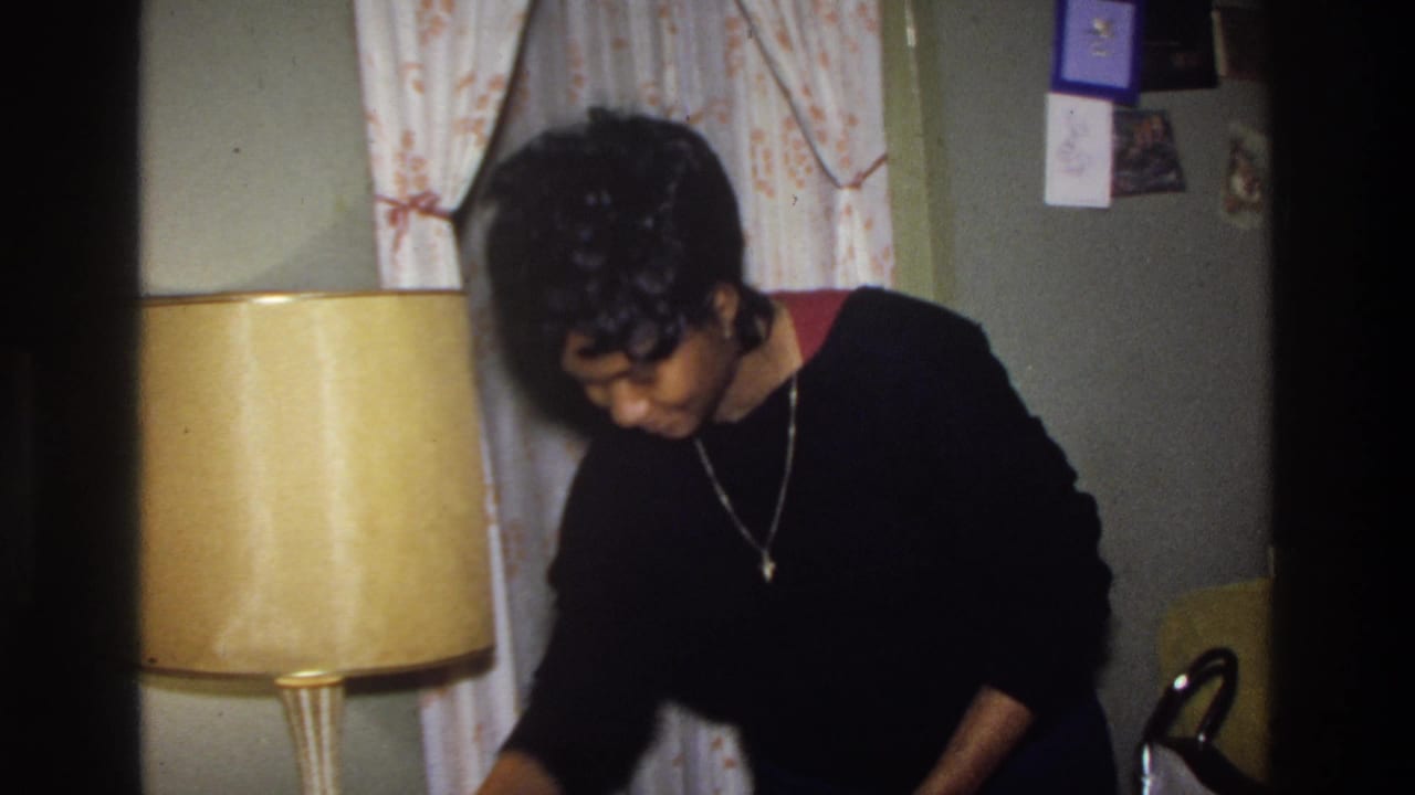 Woman in black sweater stands near a large amber cylindrical lamp with floral curtains behind her.