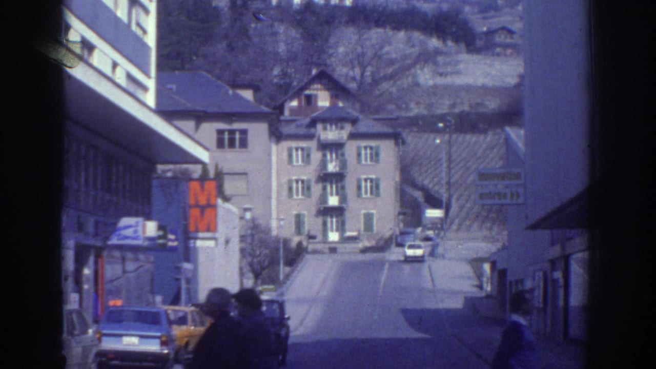 Hillside street scene with cars, pedestrians, multi-story buildings, and a prominent orange M sign on the left.