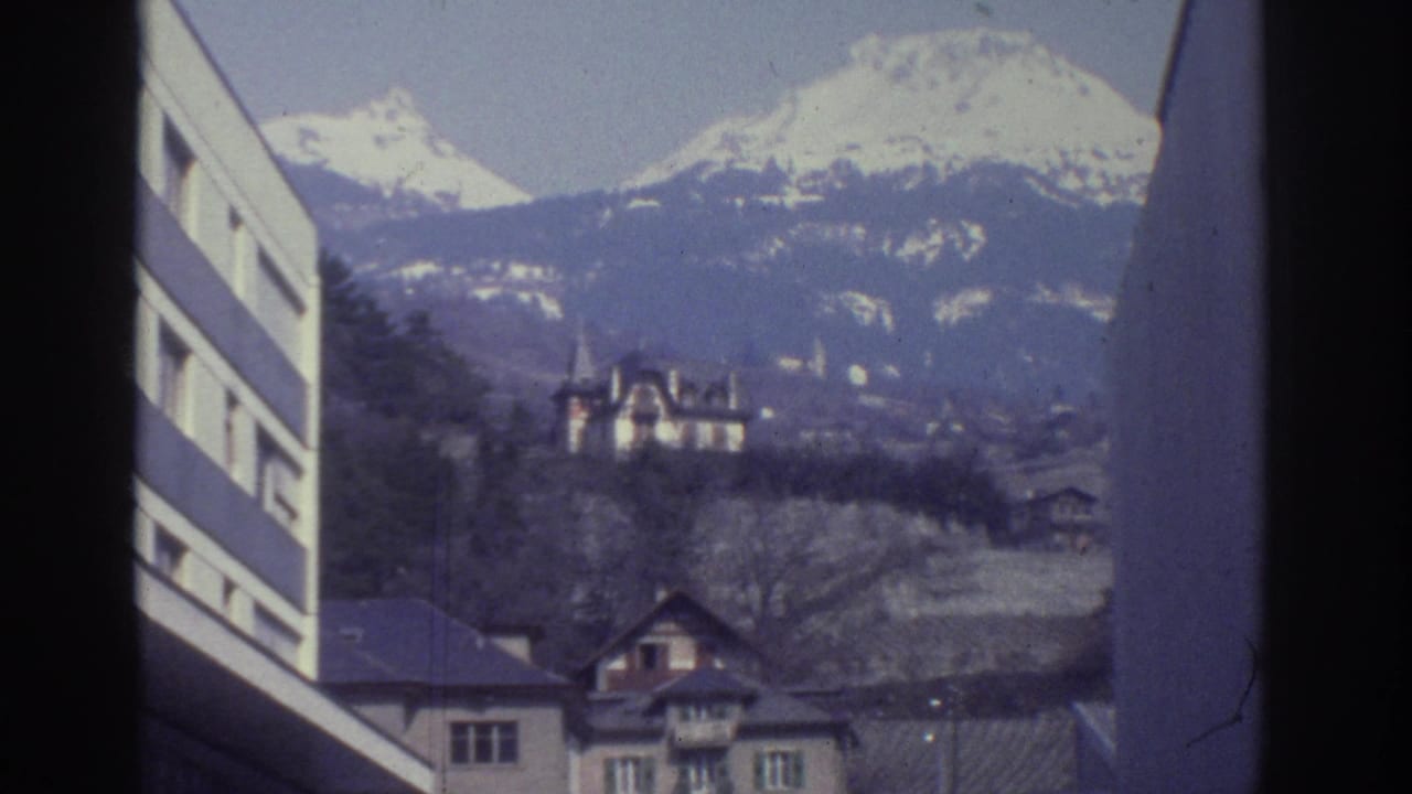 8mm frame from Bern, Switzerland, circa 1976: snow-capped peaks above a hillside chateau with pointed turrets and a layered mid-century townscape; striped building facade at left edge.