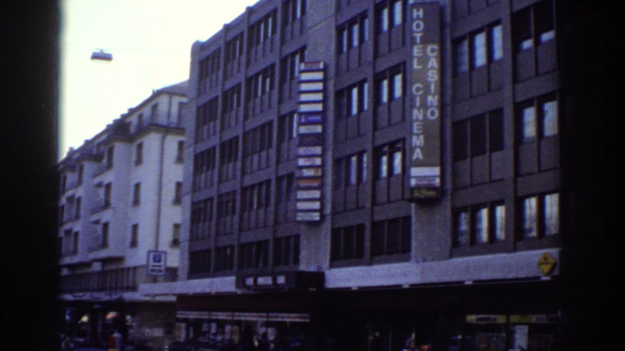 8mm frame from Bern, Switzerland, circa 1976: a commercial building carries a vertical neon sign reading 'HOTEL CASINO CINEMA'; street-level facades and a yellow sign at lower right.