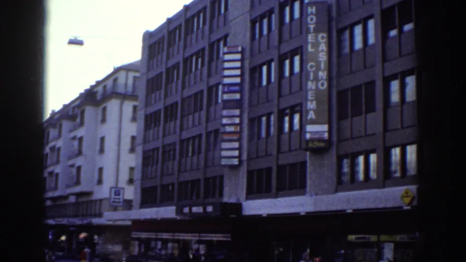 8mm frame from Bern, Switzerland, circa 1976: a commercial building carries a vertical neon sign reading 'HOTEL CASINO CINEMA'; street-level facades and a yellow sign at lower right.