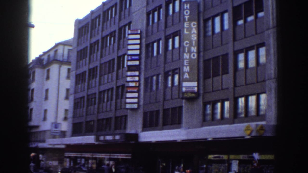 Six-story modernist building with a vertical Hotel Casino Cinema sign; pedestrians visible at street level; 8mm film.