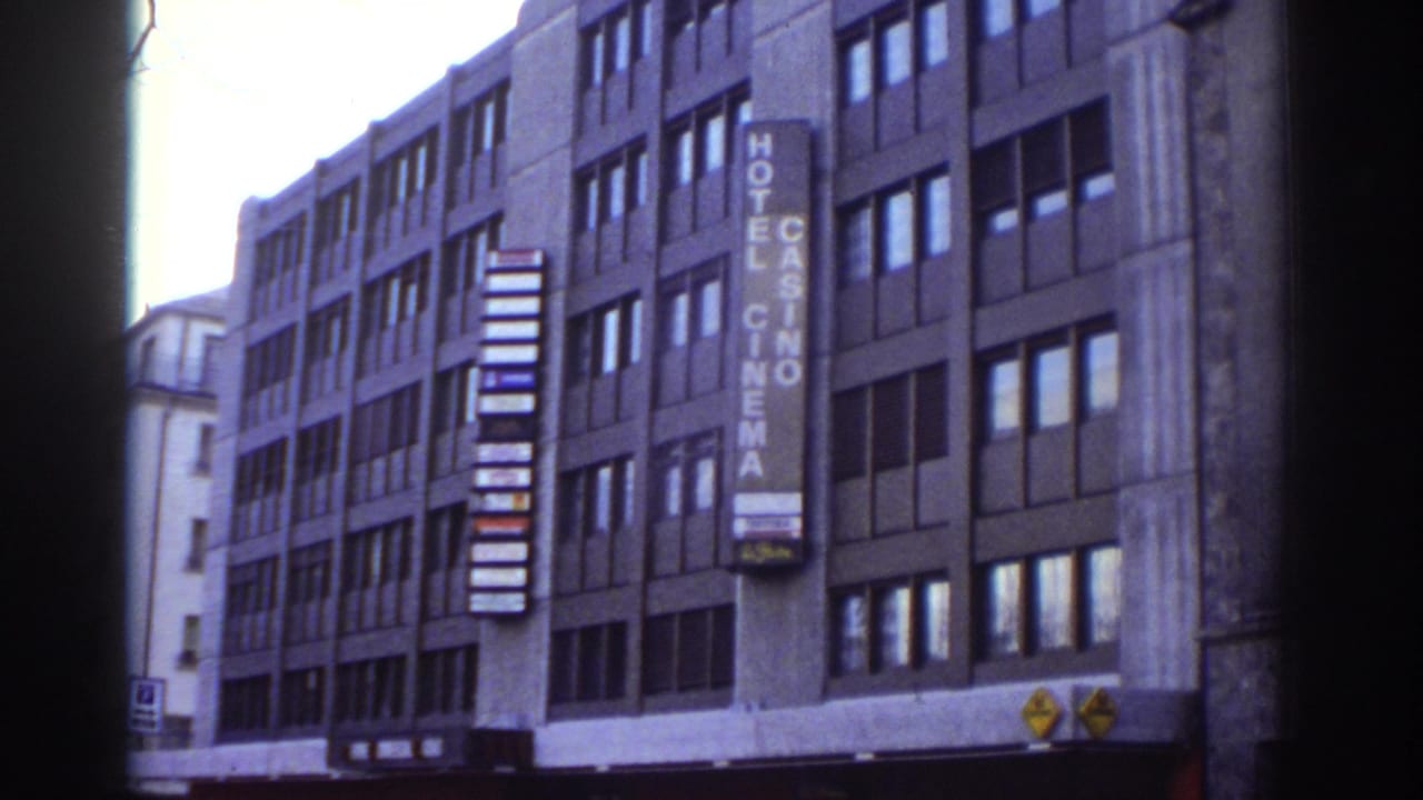 Panned view of Bern, Switzerland modernist building c.1976, showing Hotel Casino Cinema sign, concrete facade detail, and bare tree branches; 8mm grain.