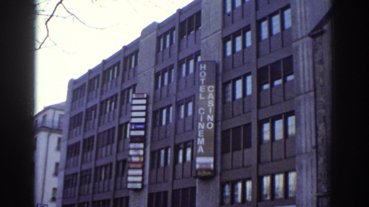 Final frame of slow pan across Bern, Switzerland building c.1976; Hotel Casino Cinema vertical sign, bare branches against overcast sky; 8mm film.