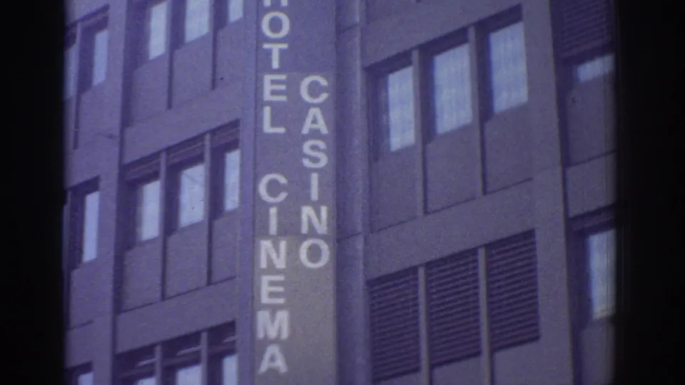 1976 Bern, Switzerland: close-up of a multi-story modernist concrete facade bearing large vertical letters spelling 'HOTEL', 'CASINO', and 'CINEMA', shot on 8mm film.