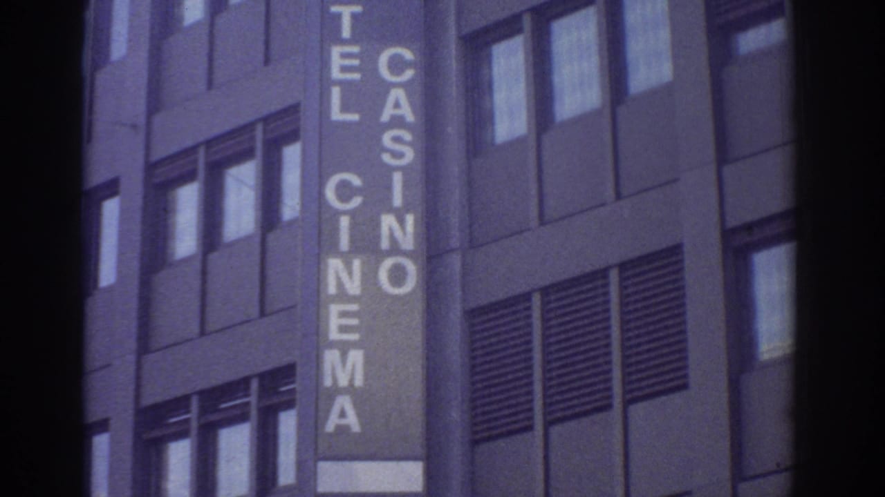 Multi-story building with vertical sign reading HOTEL CASINO CINEMA in white letters on a dark panel, upper portion only visible, muted purple-blue 8mm color.