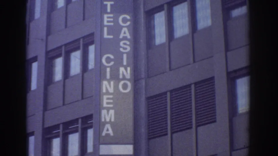 Upper section of a vertical HOTEL CASINO CINEMA sign on a mid-century modernist building facade, Bern, Switzerland, circa 1976, 8mm film with aged purple-blue color cast.