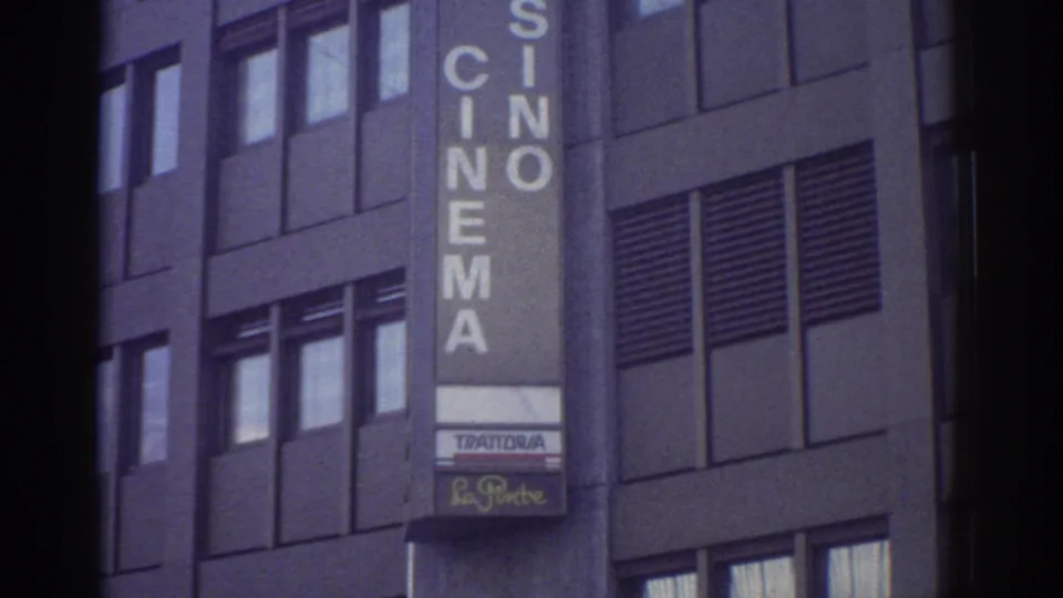 Mid-section of HOTEL CASINO CINEMA sign with Trattoria restaurant sign below on a modernist building facade, Bern, Switzerland, circa 1976, 8mm film.