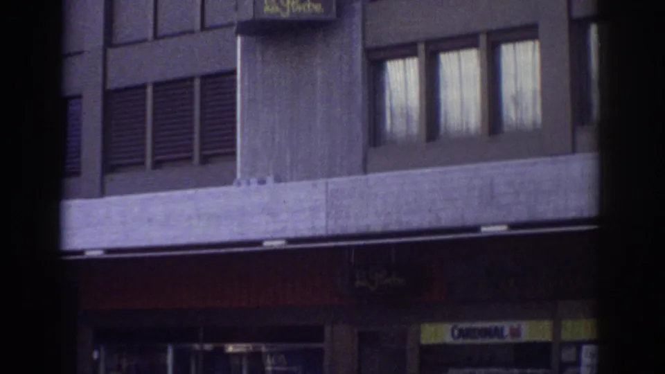 Street-level view of building base and entrance canopy with Trattoria sign and a partial yellow advertisement, Bern, Switzerland, circa 1976, 8mm film.