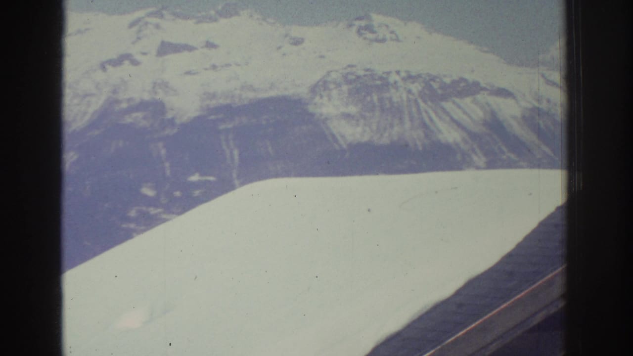 Snow-covered mountain peak filmed from a moving vehicle in what appears to be a Swiss alpine region, circa 1976, on 8mm film with characteristic color fading.