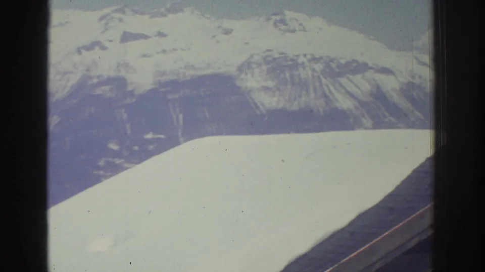 Snow-covered mountain peak filmed from a moving vehicle in what appears to be a Swiss alpine region, circa 1976, on 8mm film with characteristic color fading.